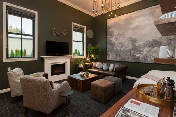 Cozy living room with dark green walls, fireplace, TV, and a wall mural of trees behind a brown sectional sofa and chairs.
