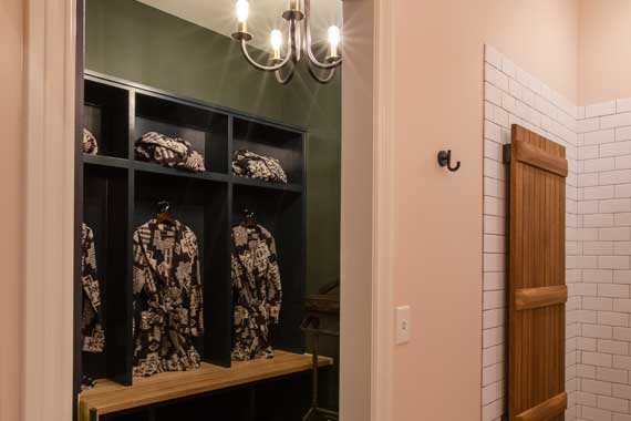 Walk-in closet display with black cubbies, hanging patterned robes, a wooden bench, and a chandelier overhead.
