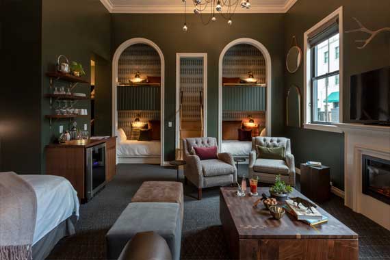 Boutique hotel suite living area with three arched bed alcoves, plush chairs, and a wooden coffee table by a fireplace.