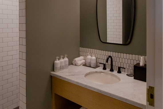Bathroom vanity with marble countertop, oval sink, black faucet, and toiletry bottles on the counter near a towel and tissue box.