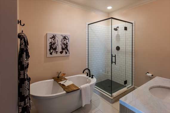 Contemporary bathroom with a freestanding oval bathtub, wooden bath tray, and towel; glass-enclosed shower with white subway tile, black fixtures, and a vanity to the right.