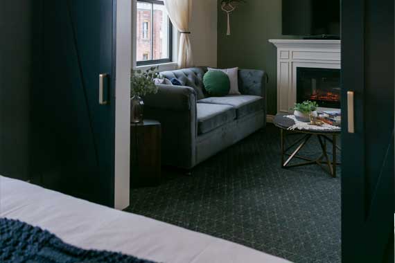 Cozy living room with a gray sofa and green pillows, seen from a doorway toward a lit fireplace.