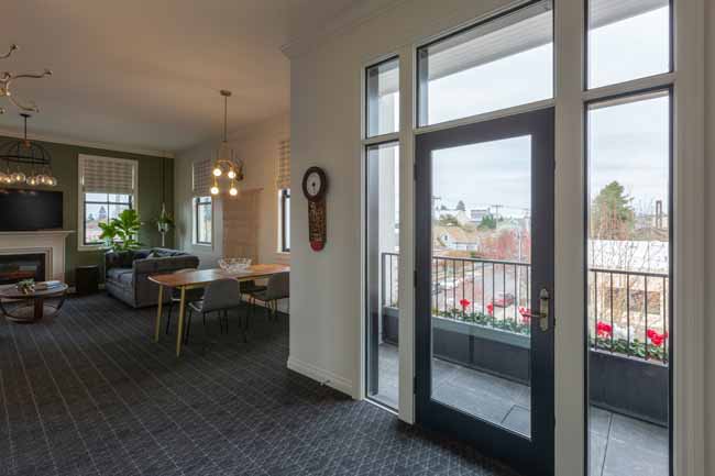 Open-plan living and dining area with a glass door to a balcony, a sofa, dining table, and a fireplace across the room.