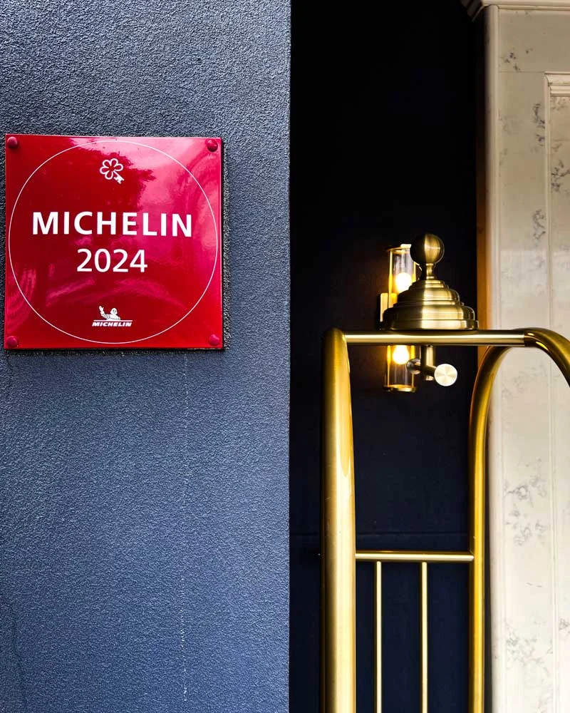 Red Michelin Guide 2024 plaque on a blue wall beside a dark doorway with a brass railing.