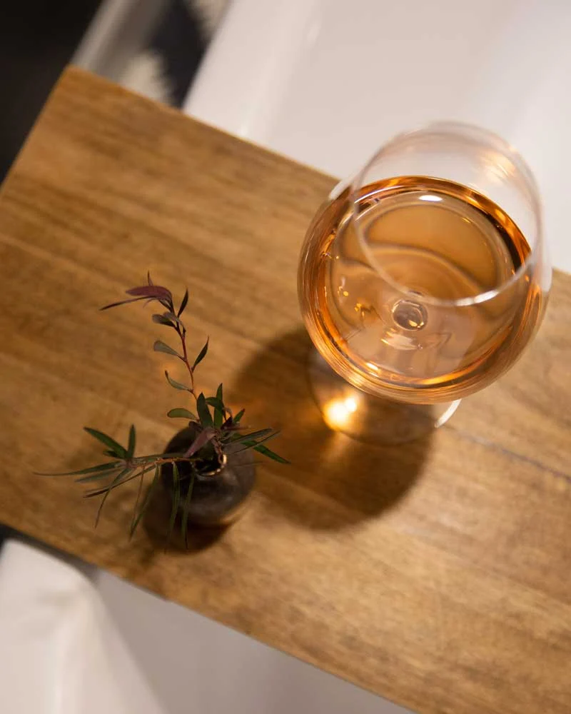 Overhead view of a wine glass with rosé on a wooden table beside a small potted plant in a dark vase.