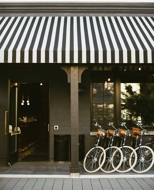 Front of a shop with a black-and-white striped awning; open door and a row of bikes parked outside.